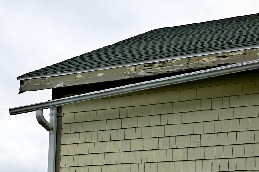 A broken gutter hanging off roof due to storm damage.